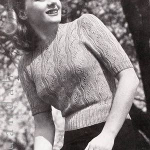 May include: A black and white photo of a woman wearing a knitted sweater with a cable stitch pattern. The sweater has short sleeves and a round neckline. The woman is smiling and looking to the side. The photo is from the 1940s and features the text "Patons & Baldwins" in the top right corner.