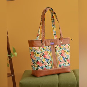 Peut inclure: Un sac fourre-tout en cuir marron avec une doublure en tissu à imprimé floral. Le sac a deux poches zippées à l'avant et deux poignées supérieures.