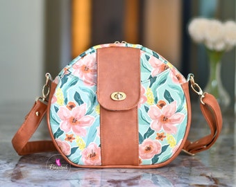 May include: A round brown and floral patterned handbag with a brown leather flap and a gold clasp. The bag has a long adjustable strap. The text "Oriana Bowler Bag" and "www.bagstockdesigns.com" is visible above the bag.