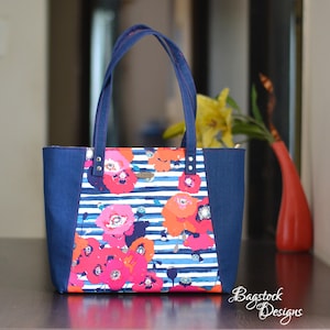May include: A blue tote bag with a white and blue striped fabric featuring a floral pattern of pink and red poppies. The bag has two navy blue straps and silver rivets.