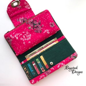 May include: A pink and green wallet with a floral print and a zipper closure. The wallet is open and shows multiple card slots and a cash compartment. The wallet is made of fabric and has a small metal loop on the top.