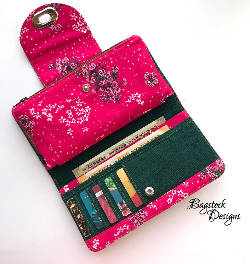 May include: A pink and green wallet with a floral print and a zipper closure. The wallet is open and shows multiple card slots and a cash compartment. The wallet is made of fabric and has a small metal loop on the top.