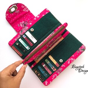 May include: A pink and green fabric wallet with a floral print and a zippered pocket. The wallet is open and has several credit cards inside.