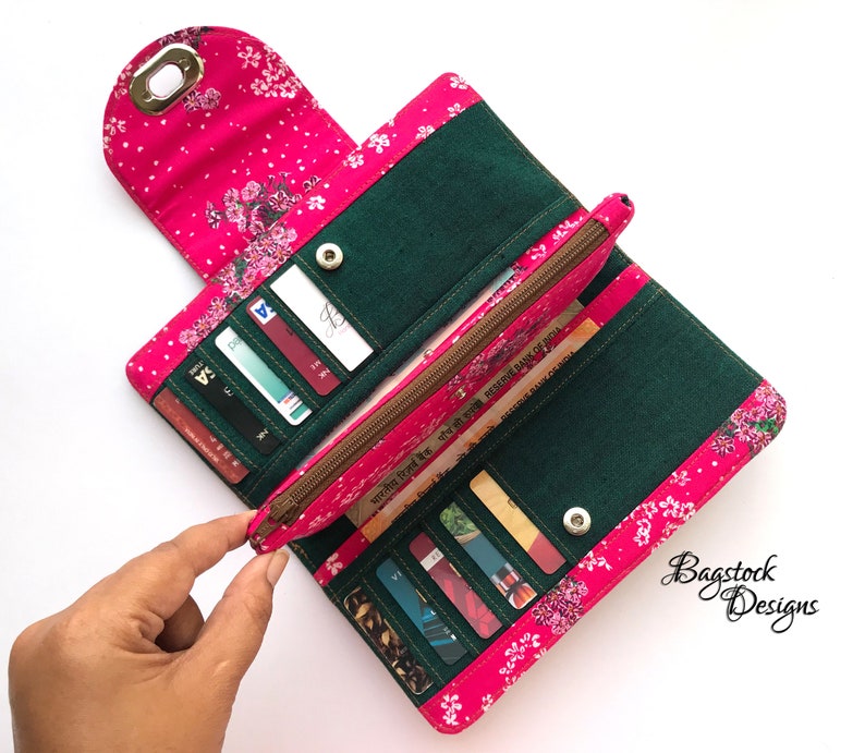 May include: A pink and green fabric wallet with a floral print and a zippered pocket. The wallet is open and has several credit cards inside.
