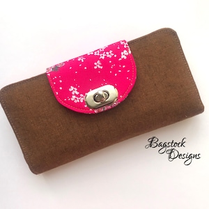 May include: A brown fabric wallet with a pink floral flap and a silver clasp. The wallet is closed and has a subtle texture.