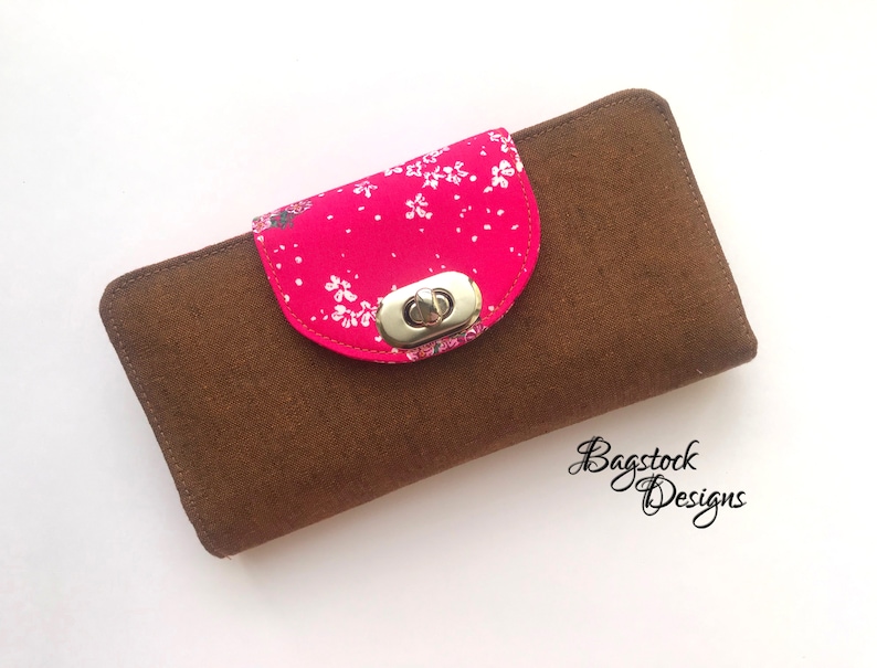 May include: A brown fabric wallet with a pink floral flap and a silver clasp. The wallet is closed and has a subtle texture.