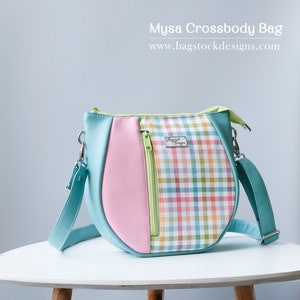 May include: A teal, pink, and green crossbody bag with a plaid pattern. The bag has a zipper closure and a small pocket on the front. The bag is made of faux leather and has a silver metal logo that says "Bagstock Designs".