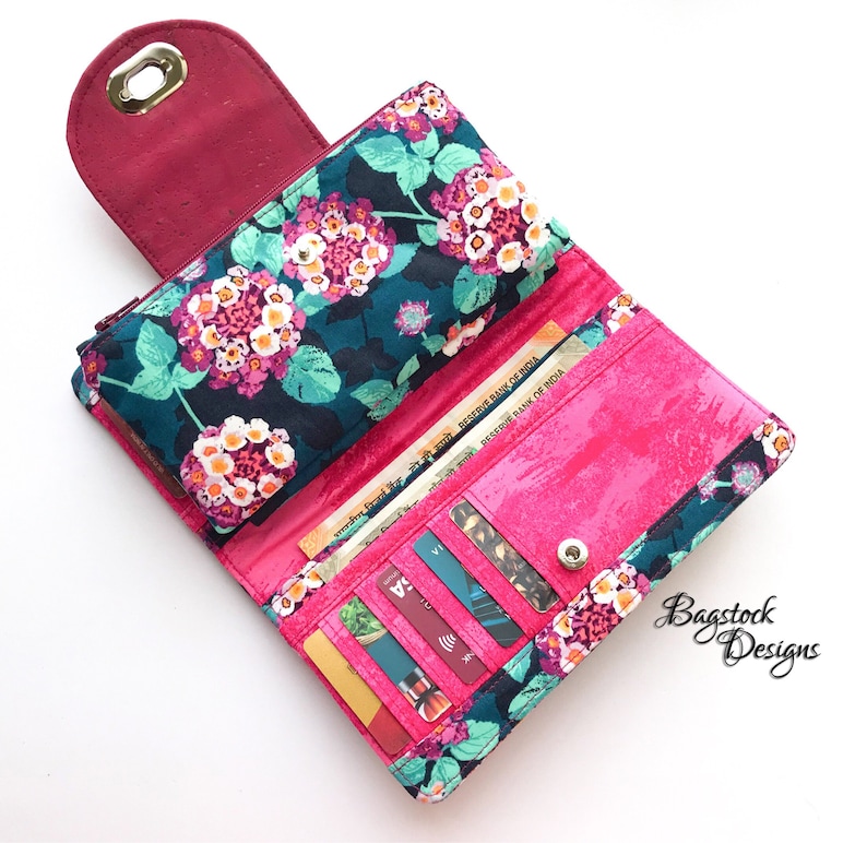 May include: A pink and teal floral wallet with a zippered closure and multiple card slots. The wallet is open and shows several credit cards and Indian rupees. The wallet is labeled "Bagstock Designs".