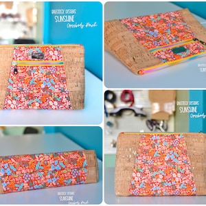 Op de afbeelding: Een crossbody tas van kurk en stof met een bloemenprint en een gele rits. De tas is gelabeld met "DAGSTOCK DESIGNS SUNSHINE Crossbody Pouch".