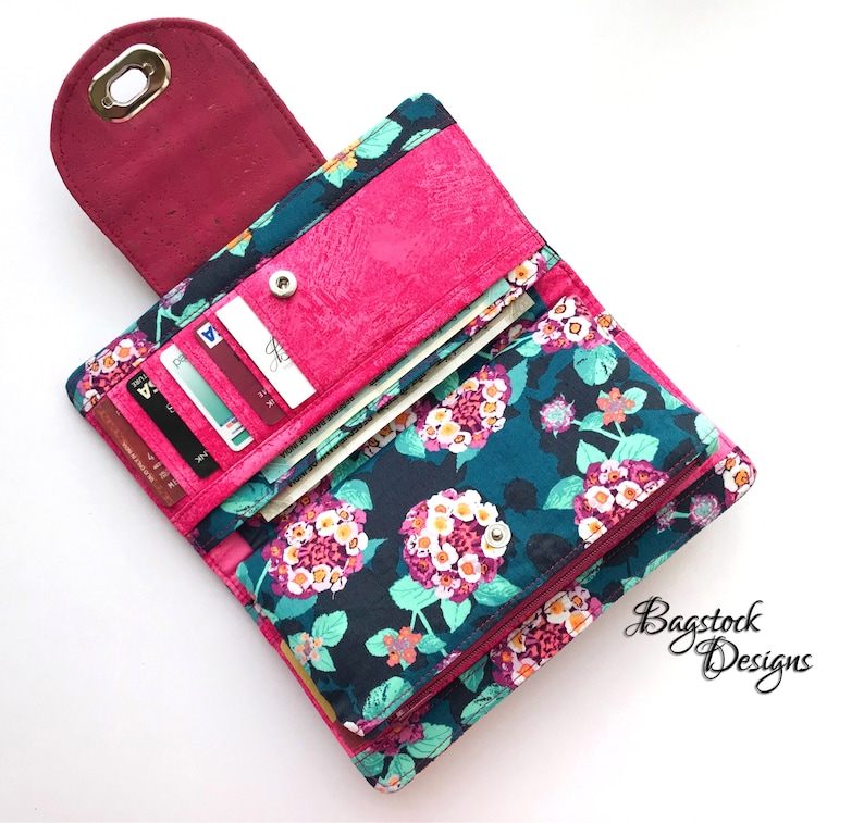 May include: A pink and teal floral patterned wallet with a zipper closure. The wallet is open and has multiple card slots and a cash compartment. The wallet is made of fabric and has a cork-like material on the inside.