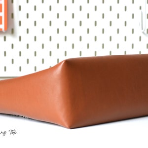 May include: A brown leather tote bag with the text "BAGSTOCK DESIGNS MYRA Shopping Tote" printed on the front.