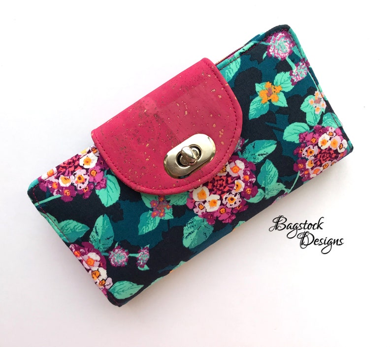 May include: A pink and teal floral print wallet with a cork and pink flap closure and a gold metal clasp. The wallet has a zipper on the top.