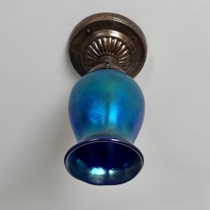 May include: A vintage ceiling light fixture with a blue iridescent glass shade. The shade has a rounded body and a flared base. The fixture is attached to a bronze-colored metal base.