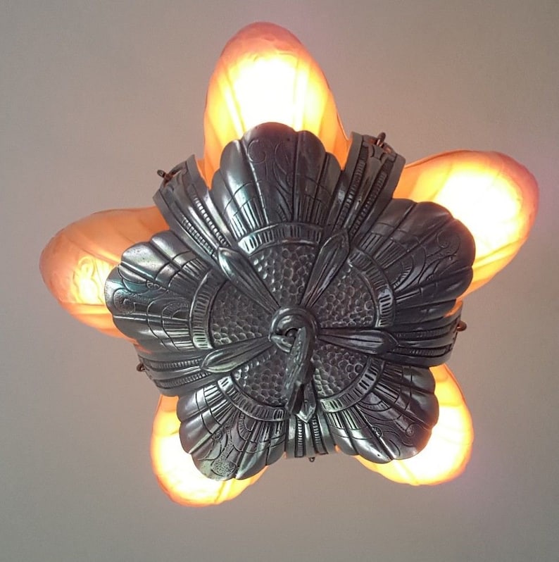 May include: A silver ceiling light fixture with a floral design and five frosted glass shades. The light fixture is lit and the glass shades are glowing.