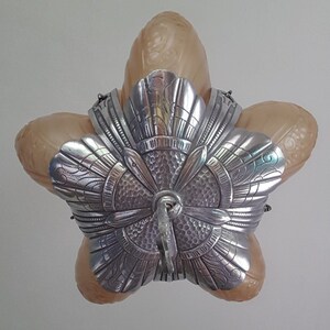 May include: A silver and glass ceiling light fixture with a five-pointed star shape. The fixture has a decorative, ornate design with a central, circular, textured element.