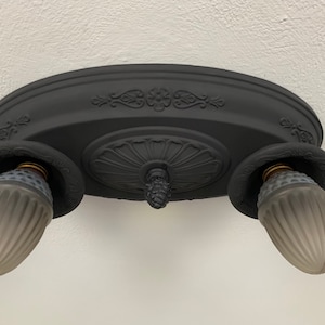 Puede incluir: Luminaria de techo negra con tres bombillas de vidrio esmerilado. La luminaria tiene una base ovalada con detalles decorativos.