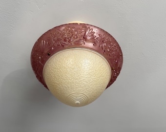 May include: A vintage ceiling light fixture with a maroon floral-patterned rim and a textured, off-white glass globe. The light is round and appears to be made of metal and glass. The fixture is mounted on a white ceiling.