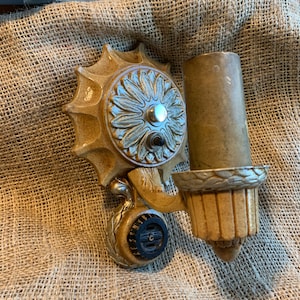 Puede incluir: Una lámpara de pared dorada y plateada con un diseño floral. La lámpara tiene una base redonda con un patrón floral decorativo y una pantalla cilíndrica.