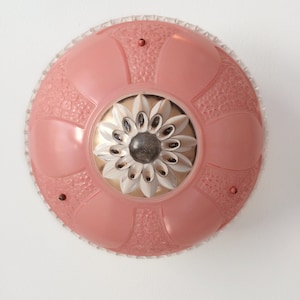May include: A vintage, round ceiling light fixture. The fixture features a pink, glass shade with a floral design and a clear, textured edge. The center has a silver and white flower design with a dark center.