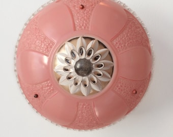 May include: A vintage, round ceiling light fixture. The fixture features a pink, glass shade with a floral design and a clear, textured edge. The center has a silver and white flower design with a dark center.
