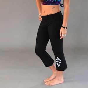 May include: A woman wearing a tie-dye hooded crop top and black yoga pants with a lightning bolt graphic on the leg.