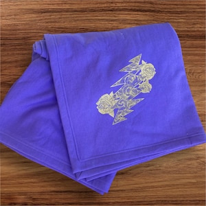 May include: A purple fleece blanket with a white embroidered design of a lightning bolt with roses.
