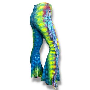 May include: Tie-dye bell-bottom pants in shades of blue, yellow, and red. The pants feature a fringe detail along the side of the leg. The fabric has a vibrant, psychedelic pattern, creating a unique and eye-catching look.