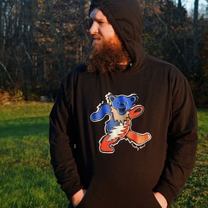 May include: A black hooded sweatshirt with a colorful graphic of a dancing bear wearing a tie-dye shirt. The bear is blue, red, white, and yellow. The text "dancing bear" is printed below the bear.