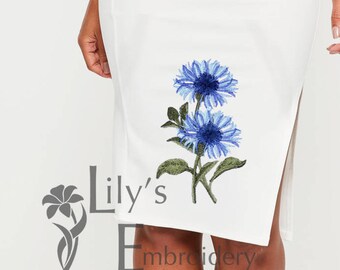 May include: White one-shoulder dress with blue embroidered flowers on the shoulder and side. The dress has a fitted silhouette and a slit on the side.