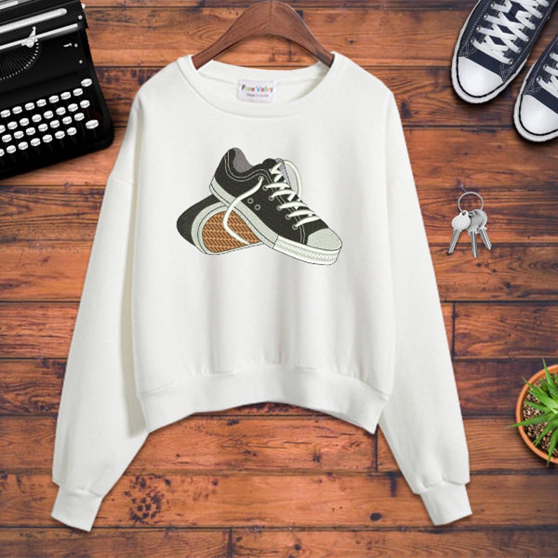Puede incluir: Sudadera blanca con un gr&aacute;fico en blanco y negro de un par de zapatillas.