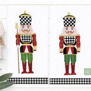May include: Two embroidered nutcracker designs with a black and white checkered hat, red and green clothing, and gold accents. The designs are on a white background with a black and white checkered border.