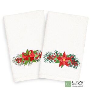 K&ouml;nnte beinhalten: Zwei wei&szlig;e Handt&uuml;cher mit gestickten Weihnachtsmotiven. Ein Handtuch zeigt eine rote Schleife mit gr&uuml;nen Kiefern&auml;sten und roten Beeren. Das andere Handtuch zeigt eine rote Weihnachtsstern mit gr&uuml;nen Kiefern&auml;sten und roten Beeren.