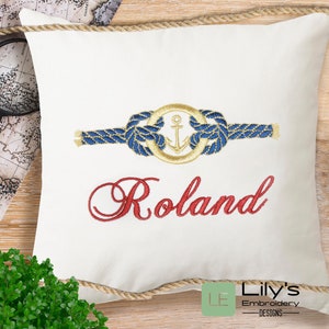 May include: White pillow with a blue and gold nautical rope design and an anchor. The name "Roland" is embroidered in red below the design.