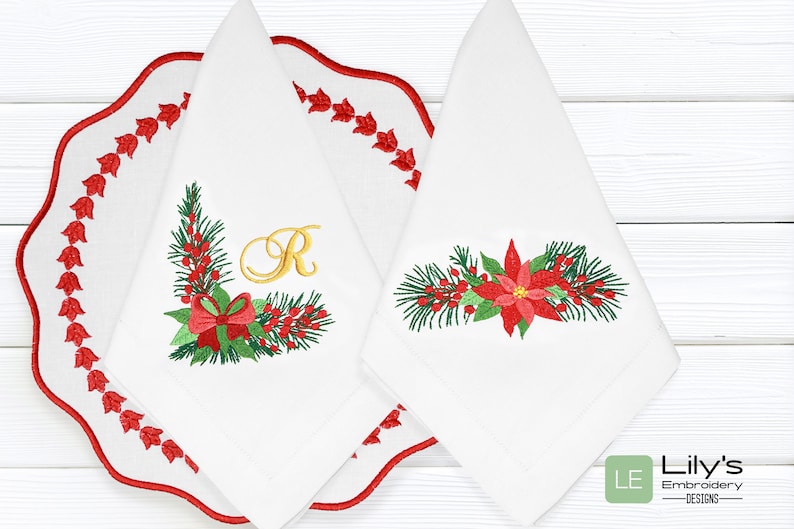 K&ouml;nnte beinhalten: Zwei wei&szlig;e bestickte Servietten mit Weihnachtsmotiv. Eine Serviette zeigt eine Weihnachtsstern-Blume und Kiefern&auml;ste, w&auml;hrend die andere einen Kranz aus Kiefern&auml;sten mit einer roten Schleife und dem Buchstaben "R" in Gold hat. Die Servietten liegen auf einer wei&szlig;en Holzoberfl&auml;che.
