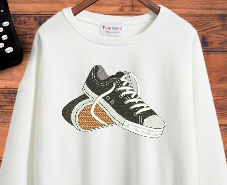Puede incluir: Sudadera blanca con un dise&ntilde;o bordado de dos zapatillas negras con cordones blancos.
