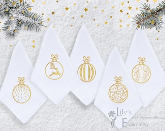 Könnte beinhalten: Fünf weiße Servietten mit goldenen gestickten Weihnachtskugeln. Die Kugeln zeigen ein Rentier, Streifen, ein Blumenmuster und ein Schneeflockenmuster. Die Servietten liegen auf einem weißen Hintergrund mit goldenen Glitzersternen.
