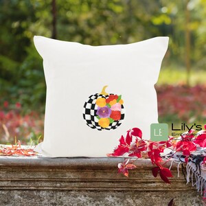 May include: A white cushion featuring a black and white checked pumpkin adorned with colourful flowers. The cushion is placed on a wooden surface with red leaves in the background. The text "Lily's Embroidery Designs" is visible in the bottom right corner of the image.