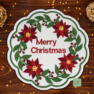 Op de afbeelding: Witte geborduurde kerstkrans met rode kerststerren en groene bladeren. De krans heeft de tekst "Merry Christmas" in het midden.