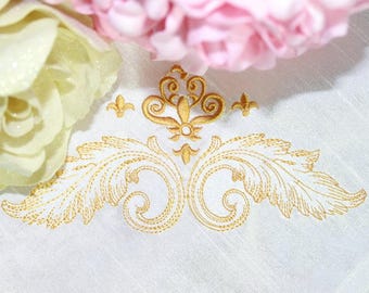 May include: White fabric with a gold embroidered design featuring a stylized floral motif. The design includes a central flourish with two symmetrical leaves on either side.