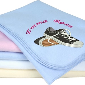 Puede incluir: Una manta de franela azul con una manta de franela rosa debajo. La manta superior tiene el nombre "Emma Rose" bordado en rosa y un par de zapatillas negras bordadas.