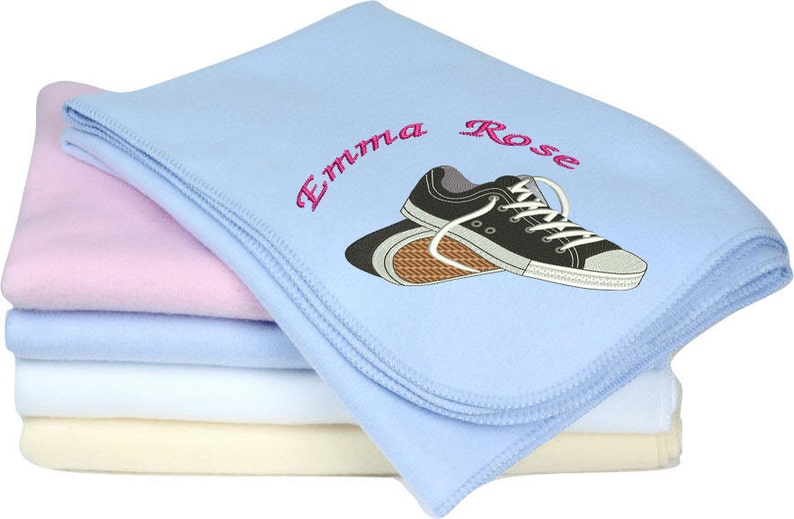 Puede incluir: Una manta de franela azul con una manta de franela rosa debajo. La manta superior tiene el nombre "Emma Rose" bordado en rosa y un par de zapatillas negras bordadas.