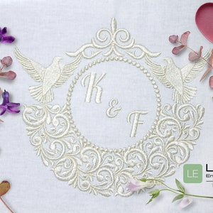 Op de afbeelding: Wit geborduurde trouwmonogram met twee duiven en een bloemmotief. Het monogram bevat de initialen "K & F".