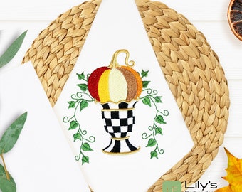Puede incluir: Diseño bordado de una calabaza en un jarrón a cuadros blanco y negro con enredaderas verdes. El diseño está en una servilleta blanca.