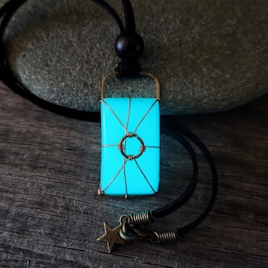 May include: A turquoise blue glass pendant with a copper wire design, hanging from a black cord with a star charm. The pendant glows in the dark.