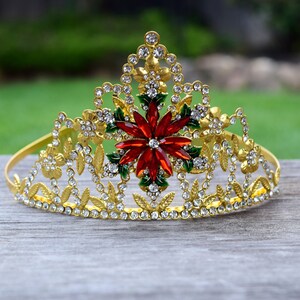 May include: A gold crown with a red and green poinsettia design and clear rhinestones.
