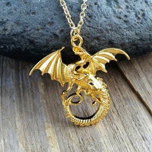 May include: A gold-toned dragon pendant necklace. The dragon is curled around itself with its wings spread out. The necklace is on a chain.