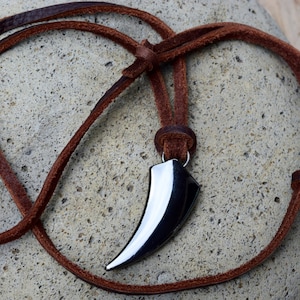 May include: A brown leather cord necklace with a silver tooth pendant.