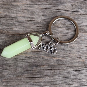 May include: A silver key chain with a green glow-in-the-dark crystal charm and a silver charm with the year 2020.