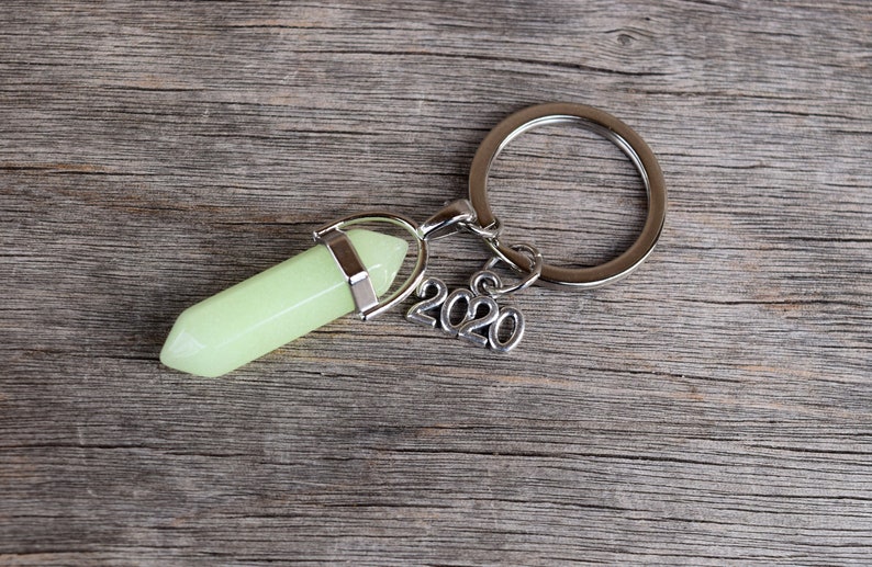 May include: A silver key chain with a green glow-in-the-dark crystal charm and a silver charm with the year 2020.