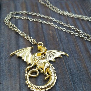 May include: A gold dragon pendant necklace with a detailed design. The dragon is curled up with its wings spread out. The necklace is on a gold chain.